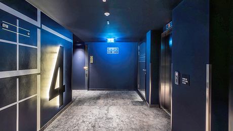 Dimly lit hotel hallway with concrete floor, dark walls, and signage directing guests.