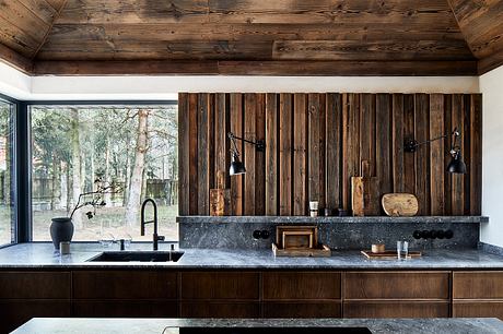 Rustic kitchen with wooden walls, dark stone countertops, and minimalist pendant lights.