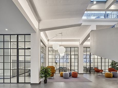 Spacious interior with exposed beams, grid-patterned windows, and colorful seating.