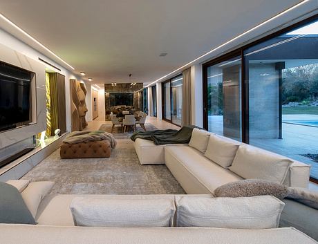 Large modern living space with a sectional sofa, statement artwork, and floor-to-ceiling windows offering a view of the pool outside.