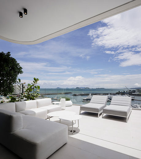 A modern, minimalist lounge with sleek white furniture and stunning views of the ocean and sky.