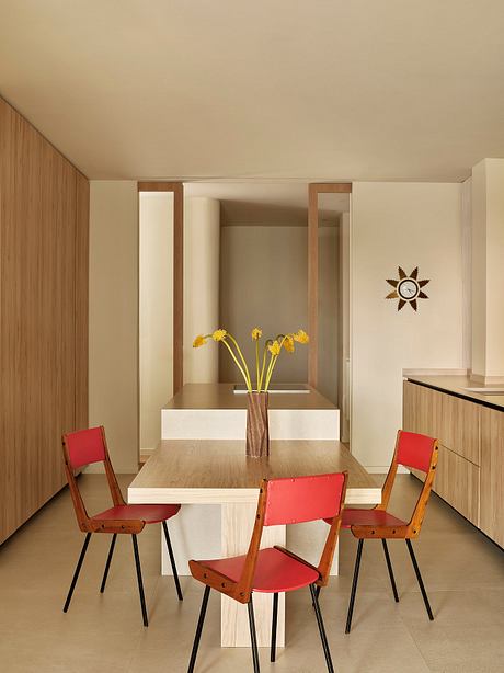 A modern dining space with a wooden table, red chairs, and a decorative wall clock.
