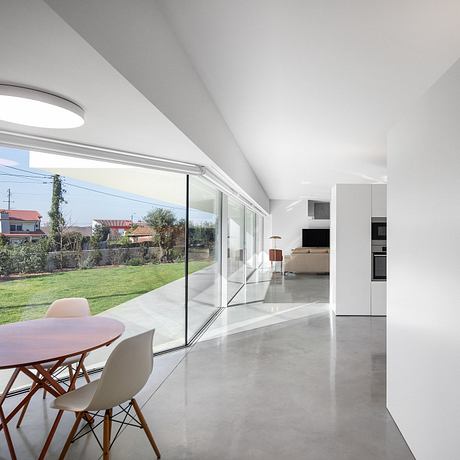 Open-concept interior with minimalist furniture, large glass doors, and a lush outdoor view.