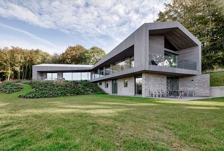 A sleek, modern house with a striking roofline, extensive glazing, and lush landscaping.
