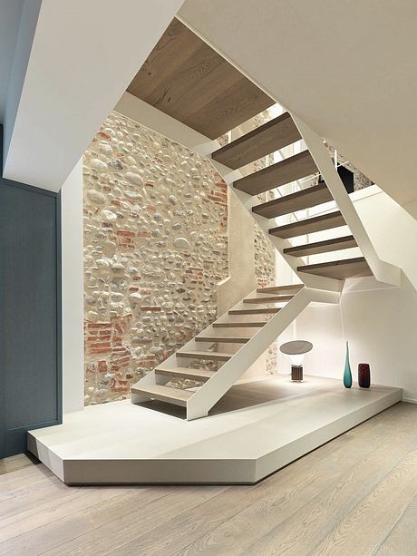 A modern staircase with wooden beams, stone wall, and minimalist decor.