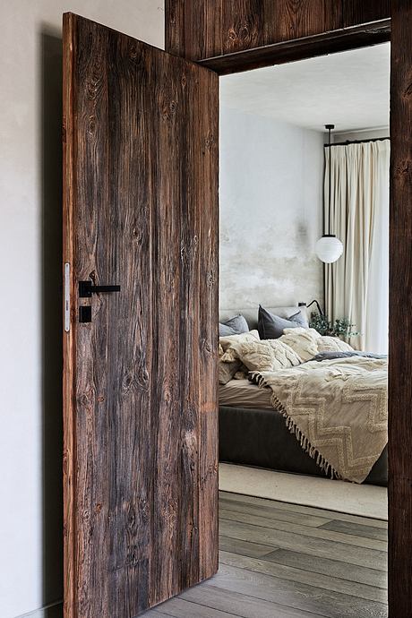 A rustic wooden door frame leading into a cozy bedroom with a plush bedding setup.