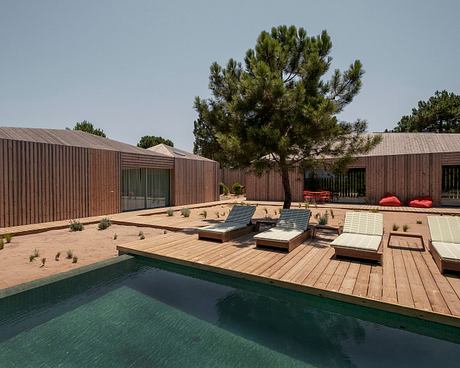 Modern wooden cabins and a wooden deck surrounding a refreshing pool, with lush greenery.