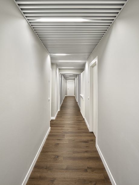 A long, minimalist hallway with wooden floors and a ceiling of parallel beams.