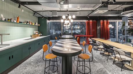 Sleek, modern kitchen with green cabinetry, hanging lights, and a communal workspace.