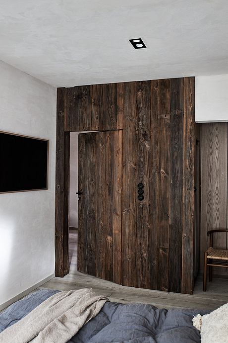 A modern bedroom with a rustic wooden accent wall and a minimalist TV setup.