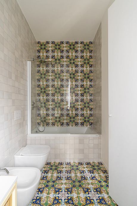 A bathroom with intricate, patterned tiles covering the walls and floor, complemented by a white toilet and bathtub.