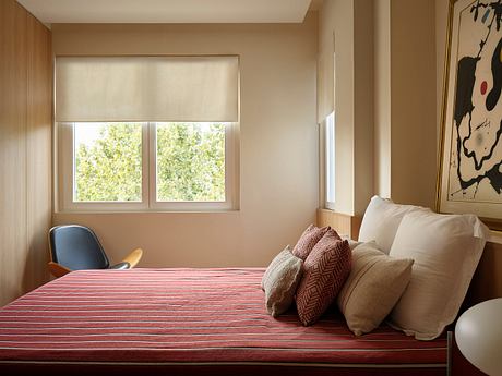Cozy bedroom with warm tones, patterned pillows, and views of lush greenery outside.