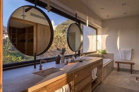 Elegant bathroom with large circular mirrors, wooden vanity, and scenic view.