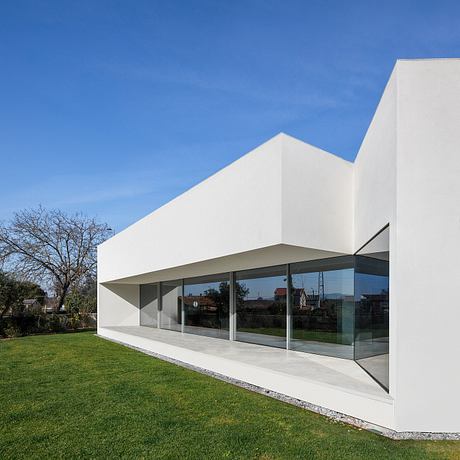 A modern, minimalist house with clean lines, large glass windows, and a grassy lawn.