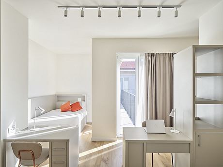 Modern, minimalist bedroom with track lighting, built-in desk, and sliding glass door.