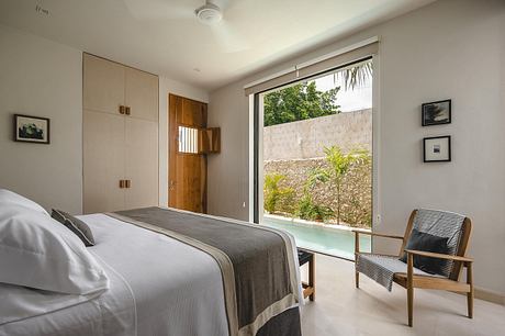 Minimalist bedroom with wooden accents, sliding glass door, and outdoor greenery view.