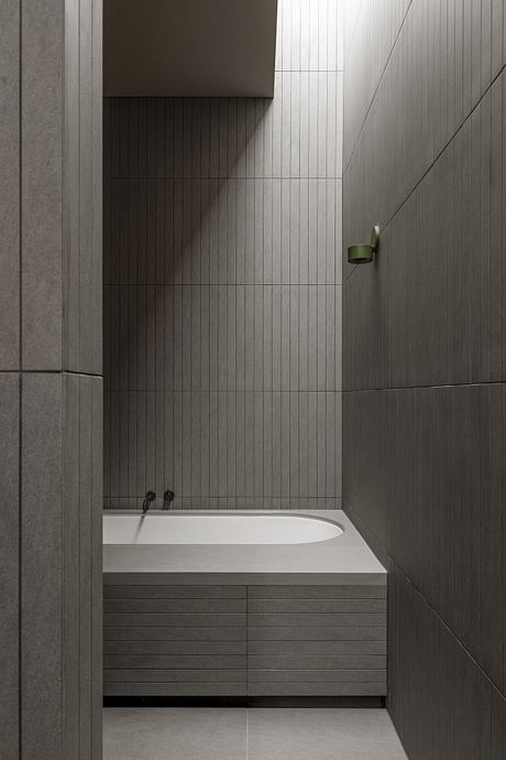 Minimalist bathroom with textured gray tiles, built-in bathtub, and a compact green accent.