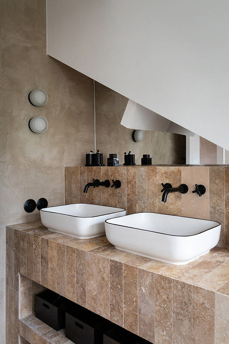 Modern bathroom with stone-tiled vanity and minimalist white vessel sinks, black faucets.