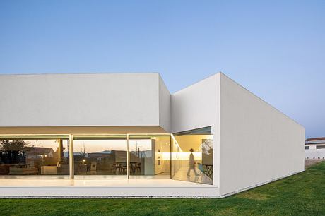 A modernist structure with large glass walls, minimalist exterior, and lawn in the foreground.