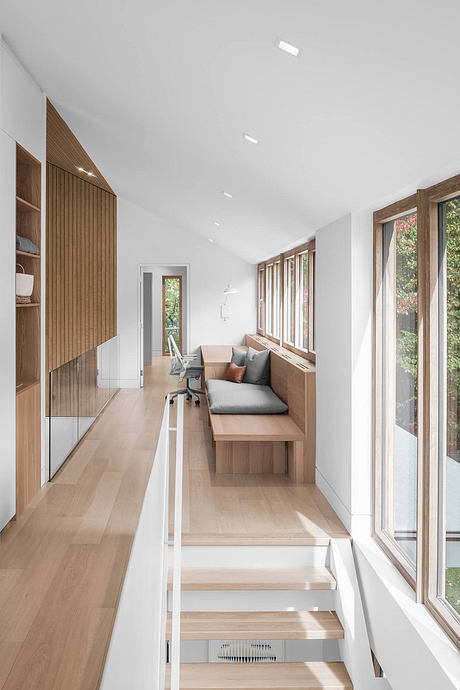 Bright, minimalist interior with wood accents, built-in seating, and large windows overlooking nature.