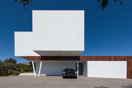 Modern white building with wooden elements and a parked car in the foreground.