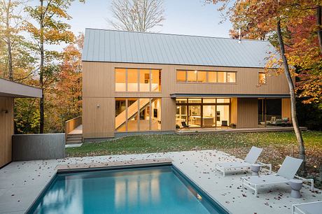 A modern two-story home with a flat metal roof, large windows, and a swimming pool surrounded by autumn foliage.