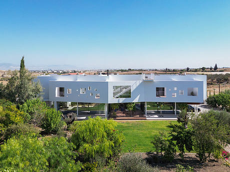 Modern white apartment building with balconies overlooking a lush green garden landscape.