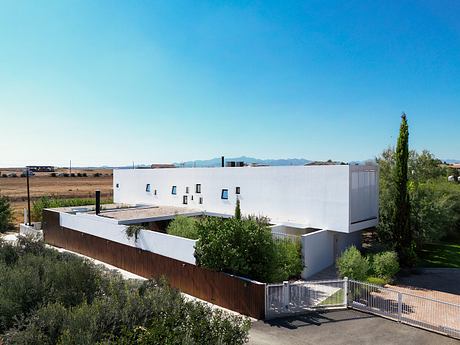 A modern, minimalist building with a white exterior, glass windows, and a wooden fence.