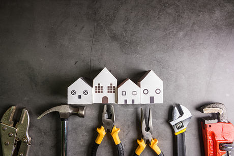 Paper houses and various tools on a dark concrete surface, suggesting architectural or home construction theme.