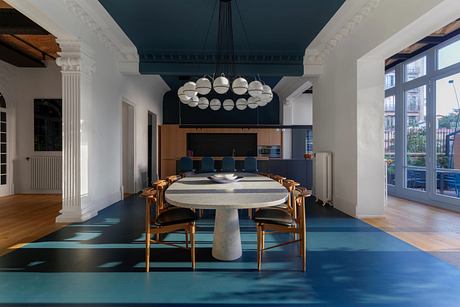 Stylish open-plan dining room with ornate chandelier, marble table, and vibrant teal floor.