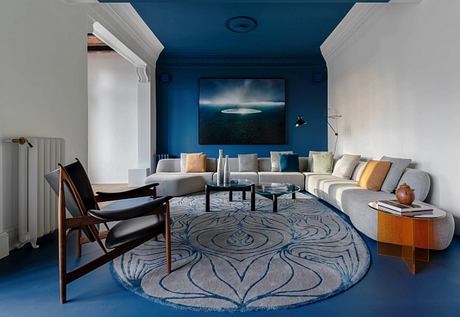 Modern, cozy living room with plush seating, bold blue walls, and a striking abstract rug.