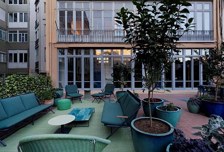 Cozy outdoor lounge area with lush greenery, plush seating, and vibrant color palette.