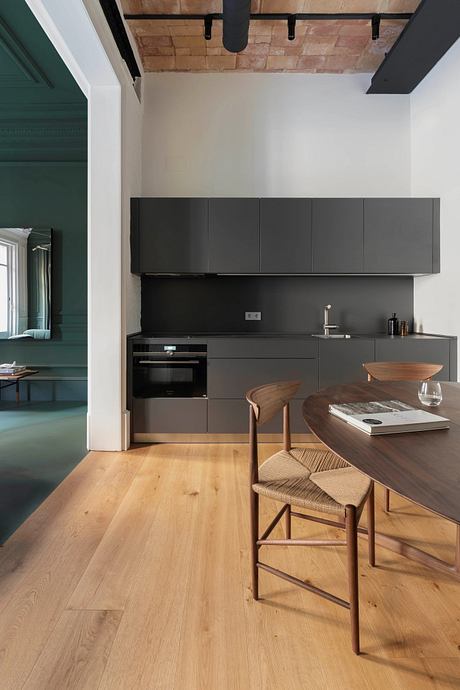 Modern kitchen with sleek black cabinetry, wooden table, and exposed brick ceiling.