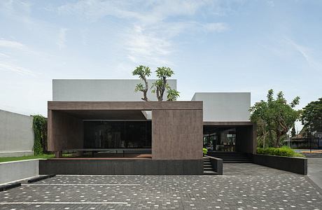 Modern, minimalist exterior with stone and glass facade, lush greenery, and paved entrance.