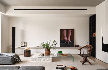 A minimalist living room featuring a glass-topped coffee table, potted plants, and an artsy wall decor.
