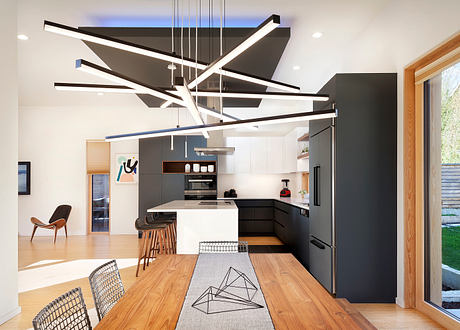 Modern, open-plan kitchen with sleek black cabinetry, geometric lighting fixture, and wooden dining table.