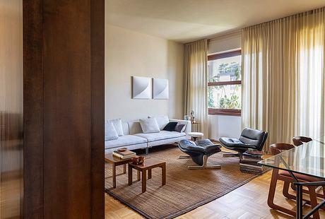Relaxing living room with large windows, wooden furniture, and a comfortable sofa.