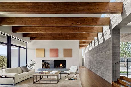 Minimalist living room with exposed wooden beams, concrete walls, and a fireplace.