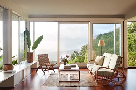 Bright, modern living room with large windows showcasing lush greenery outside.