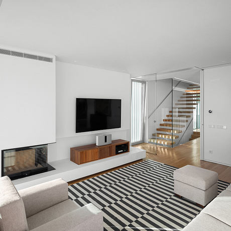 Modern living room with sleek TV stand, glass staircase, and bold striped rug.