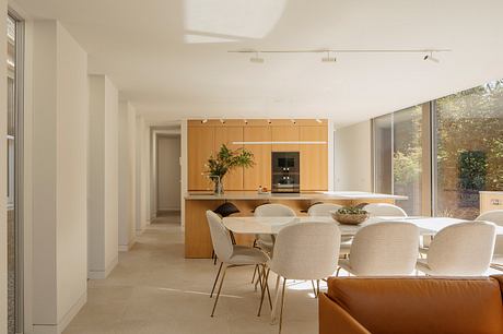 A modern, open-concept kitchen and dining area with wooden cabinetry, large windows, and neutral furnishings.