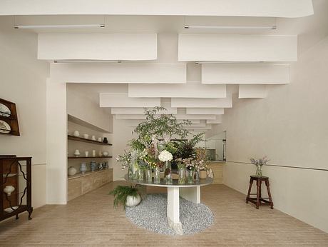 Minimalist architectural decor with elevated floral arrangement, shelves, and stool.