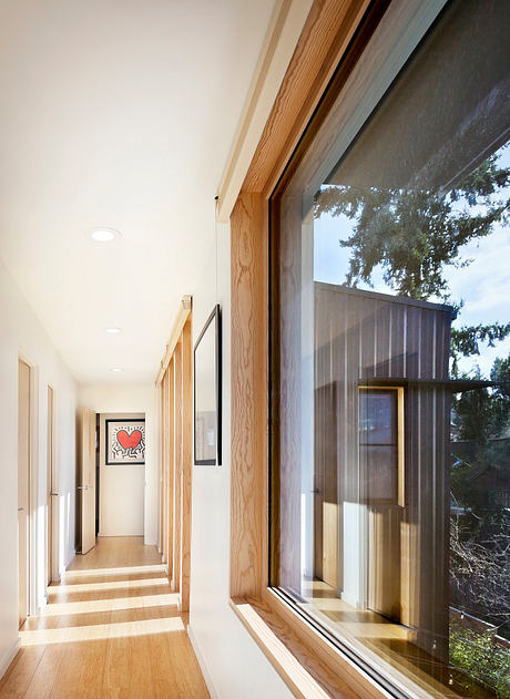 A bright, modern hallway with wooden accents, large windows, and a vibrant artwork.