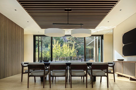 Sleek wooden ceiling beams, large windows, and a modern dining table create a warm, inviting space.
