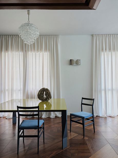Elegant dining room with a contemporary glass table, black chairs, and a crystal chandelier.