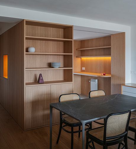 Modern open-plan kitchen with wooden cabinetry, stone dining table, and woven chairs.