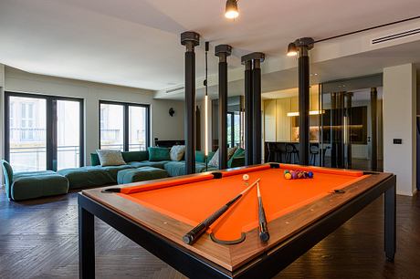 Spacious modern living room with pool table, plush green couch, and large windows.