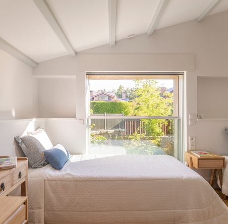 Cozy bedroom with neutral tones, large window overlooking lush greenery, and wooden accents.