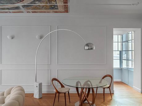 Modern dining area with circular glass-topped table, wooden chairs, and architectural wall panels.