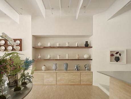 A serene, minimalist living room with built-in wooden shelving displaying ceramics.